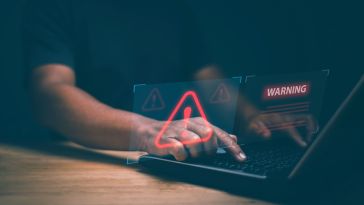 A pair of hands type on a laptop keyboard overlaid by an illustration featuring a red triangle with an exclamation mark in the center and the word WARNING to represent fraud detection.