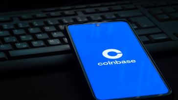A mobile device with the Coinbase logo on the screen rests on top of a desktop computer keyboard.