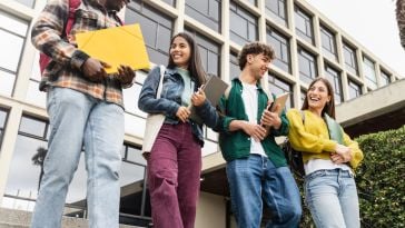 Four college students carrying notebooks are pictured smiling and laughing.