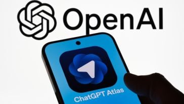Silhouette of a hand holding a smartphone with OpenAI’s Atlas on its screen, agains the background of the OpenAI logo