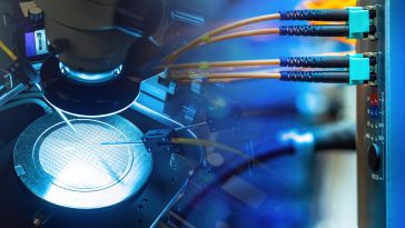 Close-up of semiconductor manufacturing equipment under a microscope, with illuminated microchips and connected fiber optic cables, conveying precision.