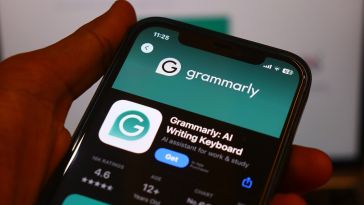 Close-up of a smartphone screen displaying the Grammarly app page in an app store. The app rating is visible, with a teal interface and a hand holding the phone.