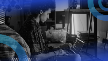 A developer works on a laptop next to a bed