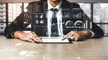 A man in a suit sits at a desk with his hands on a tablet device, and illustrations of various data charts and graphs hover over the photo.