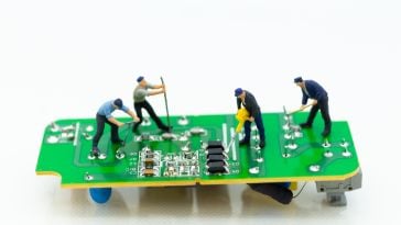A photo of miniature figures working on a circuit board to show the idea of tech advancement.