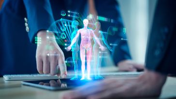 A holographic human anatomy diagram hovers over a tablet on a table. Two people in business attire are interacting with the display, highlighting medical data.