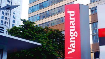Red Vanguard sign stands tall against a backdrop of modern glass buildings and lush green trees, conveying a sense of urban professionalism.