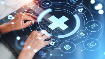 Hands typing on a laptop with medical icons and a glowing cross overlay. Represents healthcare technology and digital innovation.