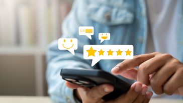A person in a denim jacket taps a smartphone screen, surrounded by floating icons of five stars, smiley faces, and a 5.0 rating, conveying satisfaction.
