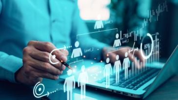 Person's hand pointing at a holographic organizational chart and data analytics overlay on a laptop and smartphone, representing business strategy and human resources.