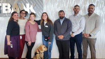 Members of FirstBank’s Veterans Employee Resource Group (ERG), one of whom is accompanied by a service dog, pose for a group photo in the company’s office