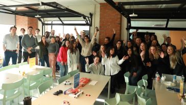 Zeta Global team members pose for a large group photo with their hands raised in the air in the company’s office