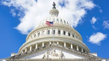 Image of looking up at the U.S. Capitol building with an American flag waving. 