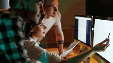 Three software engineers review lines of code while working on a project together in an office