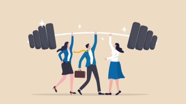 A businessman and two businesswomen raise a giant barbell over their heads, symbolizing the idea of business strength