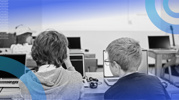 Two kids work on laptops in a classroom