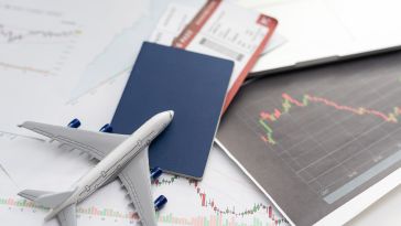 A toy airplane rests on a passport and boarding passes atop financial charts, suggesting business travel. The tone is professional and analytical.