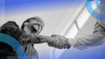 A man in a hardhat and flannel shirt shakes hands with a man in a dress shirt