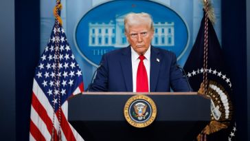 Image of Trump standing behind a podium, with an American flag in the background.
