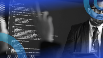 A woman asks a question of an engineer in front of a screen displaying code