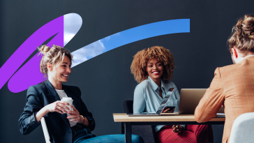 Two smiling Udemy team members chat while working together in the company’s office