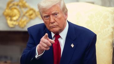 Image of President Trump pointing in front of him, wearing a blue suit and red tie with a white collar shirt.