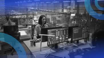 IT workers on terminals in an office with glass walls