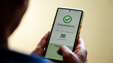 A close up of hands holding a mobile phone with a green checkmark on the screen and text stating "Congratulations! You've earned 20 points" to represent commerce rewards.