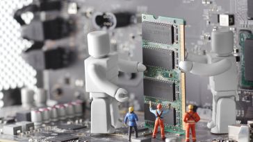 Miniature construction workers on a motherboard with two large robots to show the idea of working alongside automation and AI. 