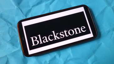 Smartphone displaying the word "Blackstone" in white text on a black rectangle, placed on crumpled blue paper. The tone is modern and sleek.