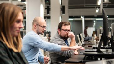 Three Prosodica employees look at a computer screen in a candid photo. 