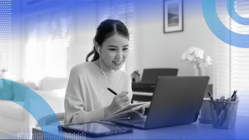 A young woman works on a laptop and writes in a notepad