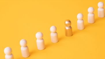 A photo of wooden figures in a line and one gold one to show the idea of working toward promotion.