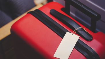 Red suitcase with a black handle and a blank white luggage tag attached. The scene suggests travel or preparation for a trip.
