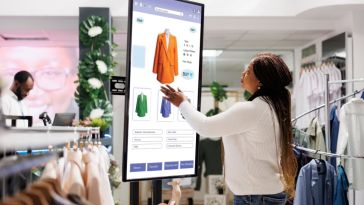 Women interacts with tech display in retail store.