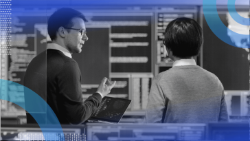 Two engineers talk with a tablet computer in front of servers