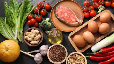Various food ingredients including eggs, fish, tomatoes and broccoli are spread across a table.