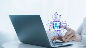 Hand typing on a laptop with a purple and blue illustration featuring the text "Ai" hovering over the computer.