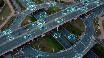 An aerial view of a multi-level highway where several cars are highlighted by glowing teal concentric circles connected by lines, representing an autonomous traffic system.