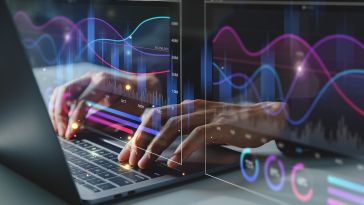 A close up of two hands typing on a laptop keyboard overlaid by a glowing digital illustration of charts and graphs.