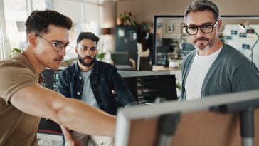 Three software engineers brainstorm ideas on a whiteboard while working on a project together in an office