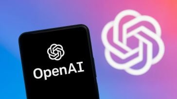 A smartphone with the OpenAI logo is pictured in front of a larger image with the OpenAI logo.