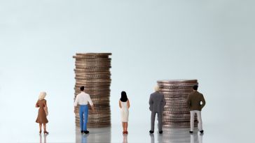 Miniature figures stand in front of two stacks of coins to show the idea of financial perks and benefits at work. 