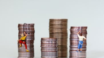 A photo of miniature  figures climbing stacks of coins to show the idea of fair and equitable pay.  