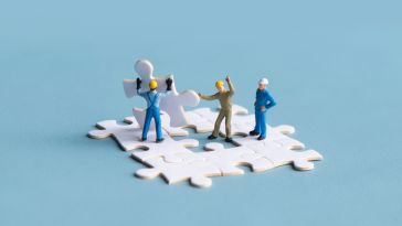 A photo of miniatures placing a puzzle piece into place to show the idea of team culture 