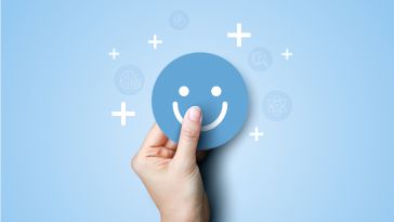 A hand holding a smiley face on a blue background to show the idea of happy employees. 