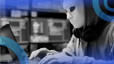 A scammer wears a mask and works on a laptop
