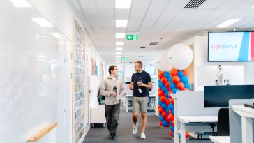 Two CarGurus employees chat while walking past desks in the company’s Dublin office