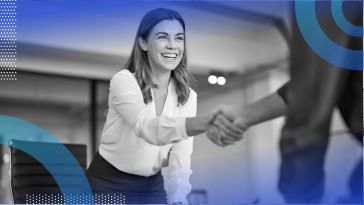 A woman smiles and shakes hands over a desk