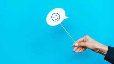 A photo of a hand holding a small sign with a smiley face to show the idea of happy employees. 